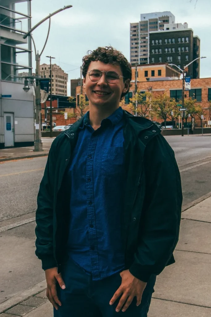 Samuel Smusiak, Windsor SEO strategist, smiling on a city sidewalk in a navy jacket and blue shirt.